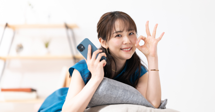 片手でスマホを持ちもう片方の手でOKサインを作っている女性