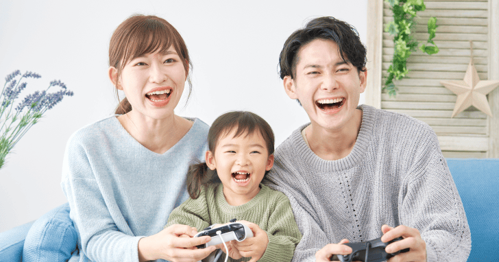 親子3人でゲームコントローラーを持ち笑っているイメージ