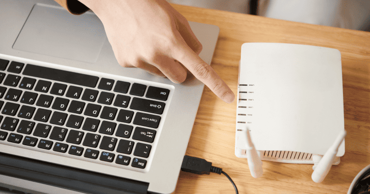 ノートパソコンの横にある無線LANルーターを指さしている様子